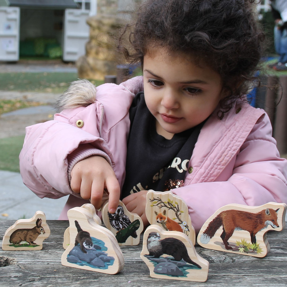 Child playing with wooden animal figurines outdoors