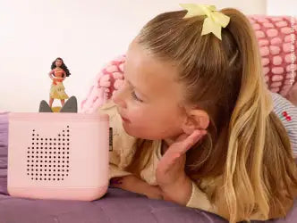Child listening to a pink toniebox 2 with a character on top, sitting on a pink couch.