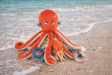 Plush octopus toy on a beach with ocean waves in the background